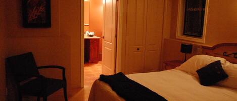 Ein Hotelzimmer mit einem Bett, einem Sessel, einem Schreibtisch mit Lampe und einer Tür zu einem weiteren Raum.