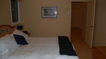 A bedroom with a bed, a nightstand, a lamp, a framed picture on the wall, and a door leading to another room.