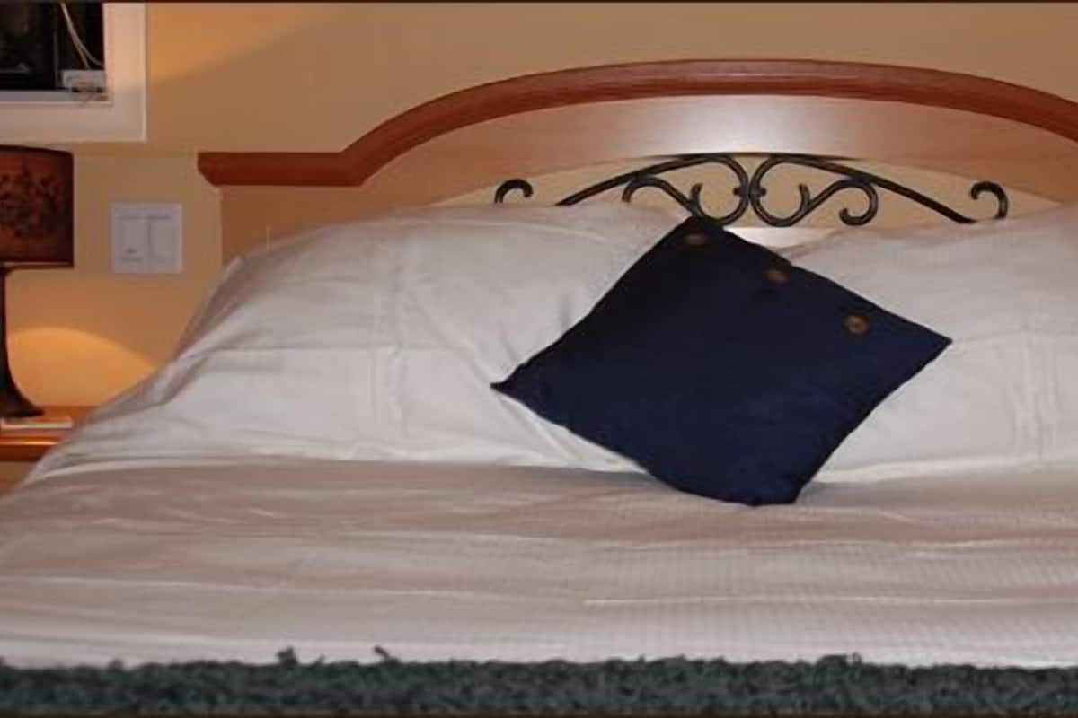 Un lit bien fait, avec des draps blancs et un oreiller bleu foncé, flanqué de deux lampes de chevet dotées d'abat-jour.