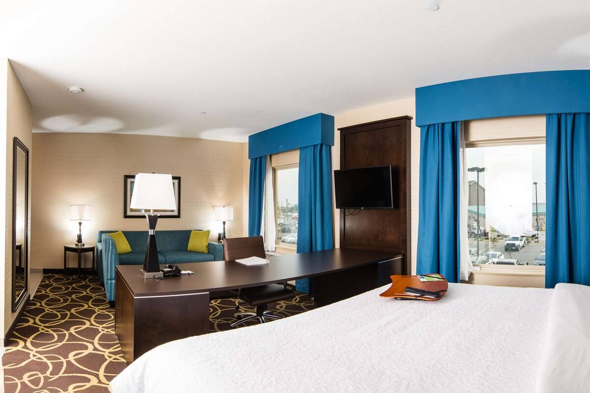 A hotel room with a large bed, a desk, a sofa, and a TV.