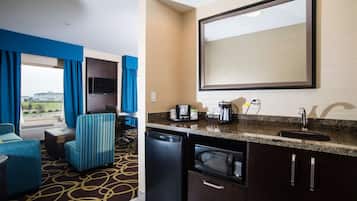 A hotel room with a kitchenette, a flat-screen TV, a large mirror, a sofa, and a view of the outdoors.