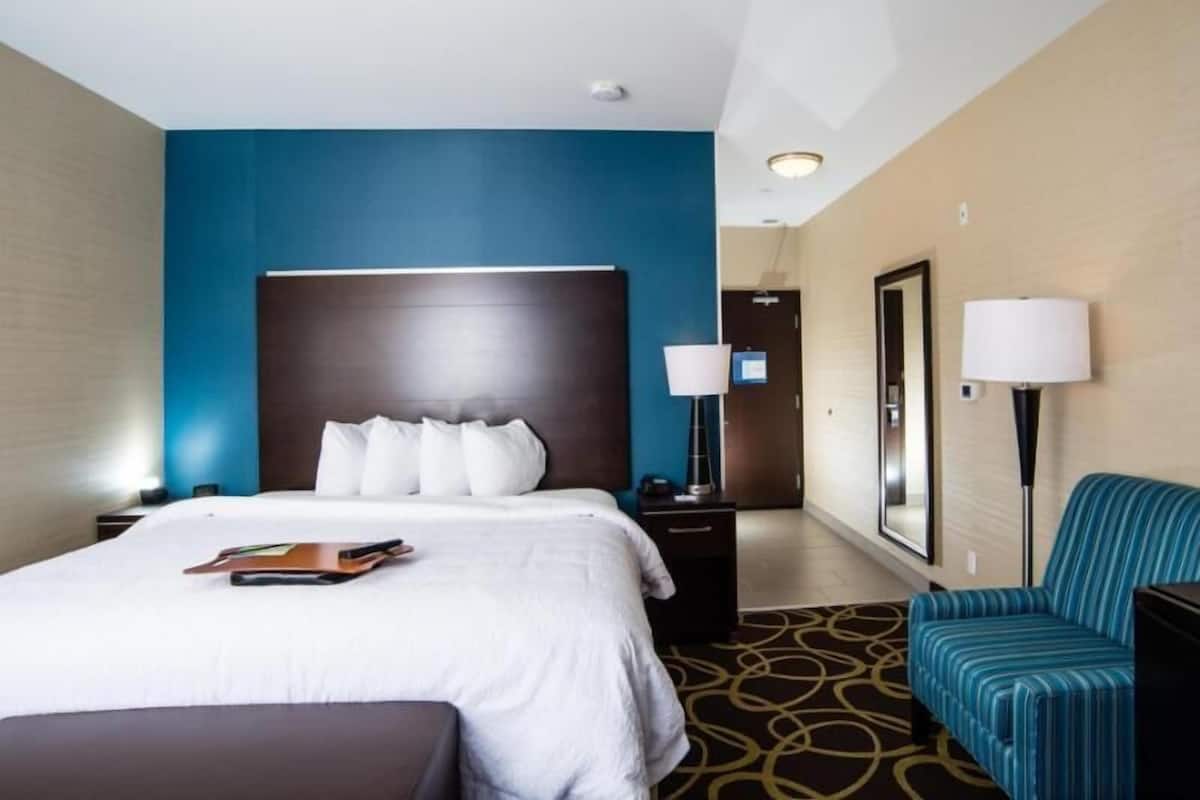 A hotel room with a large bed, a nightstand, a desk, a chair, and a lamp.