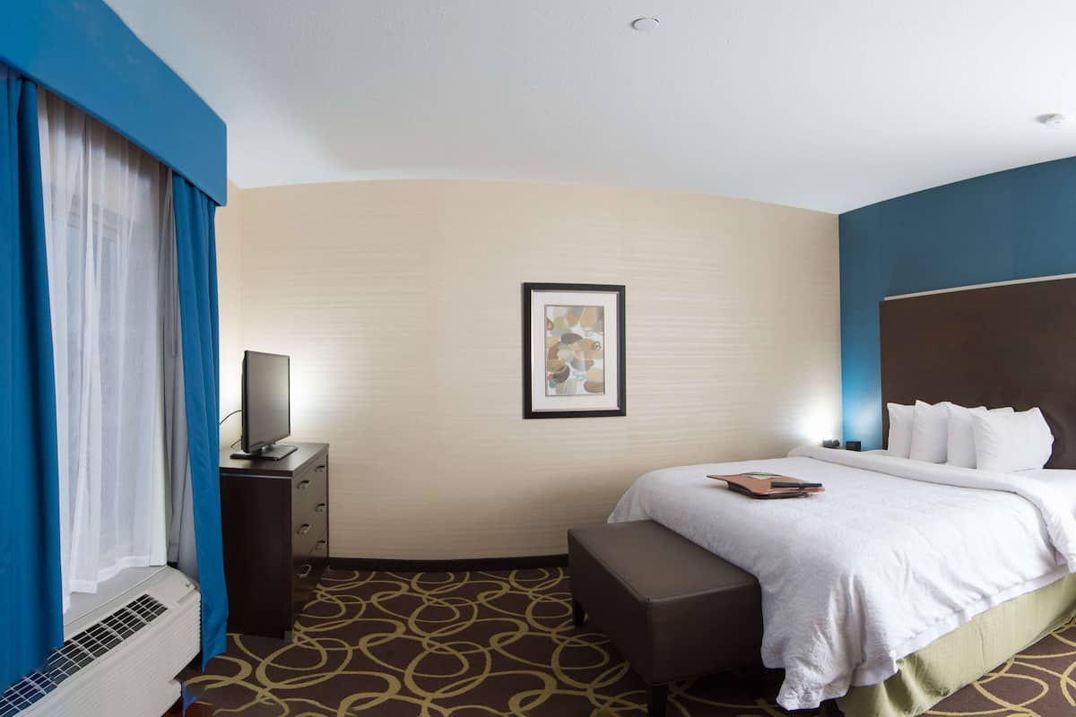 A hotel room with a bed, bedside table, lamp, and a framed picture on the wall.