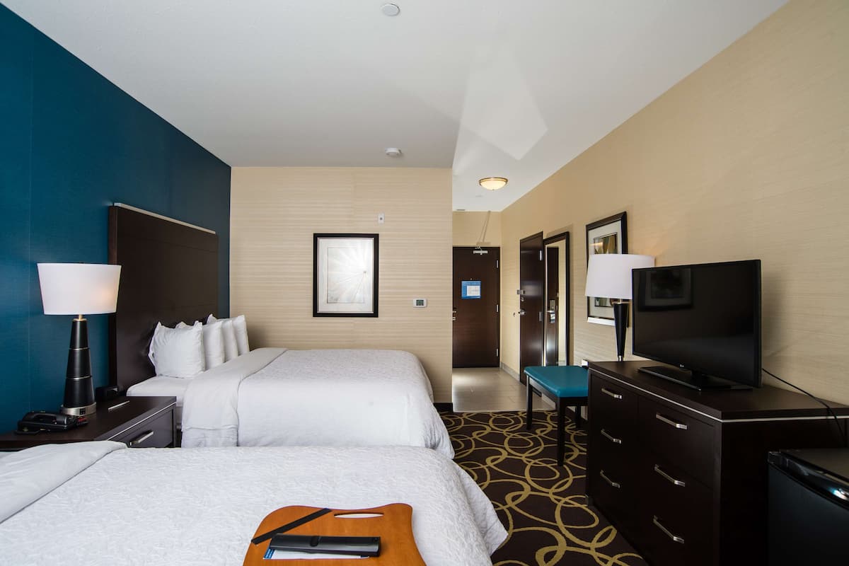 A hotel room with two beds, a TV, a desk, and a dresser.