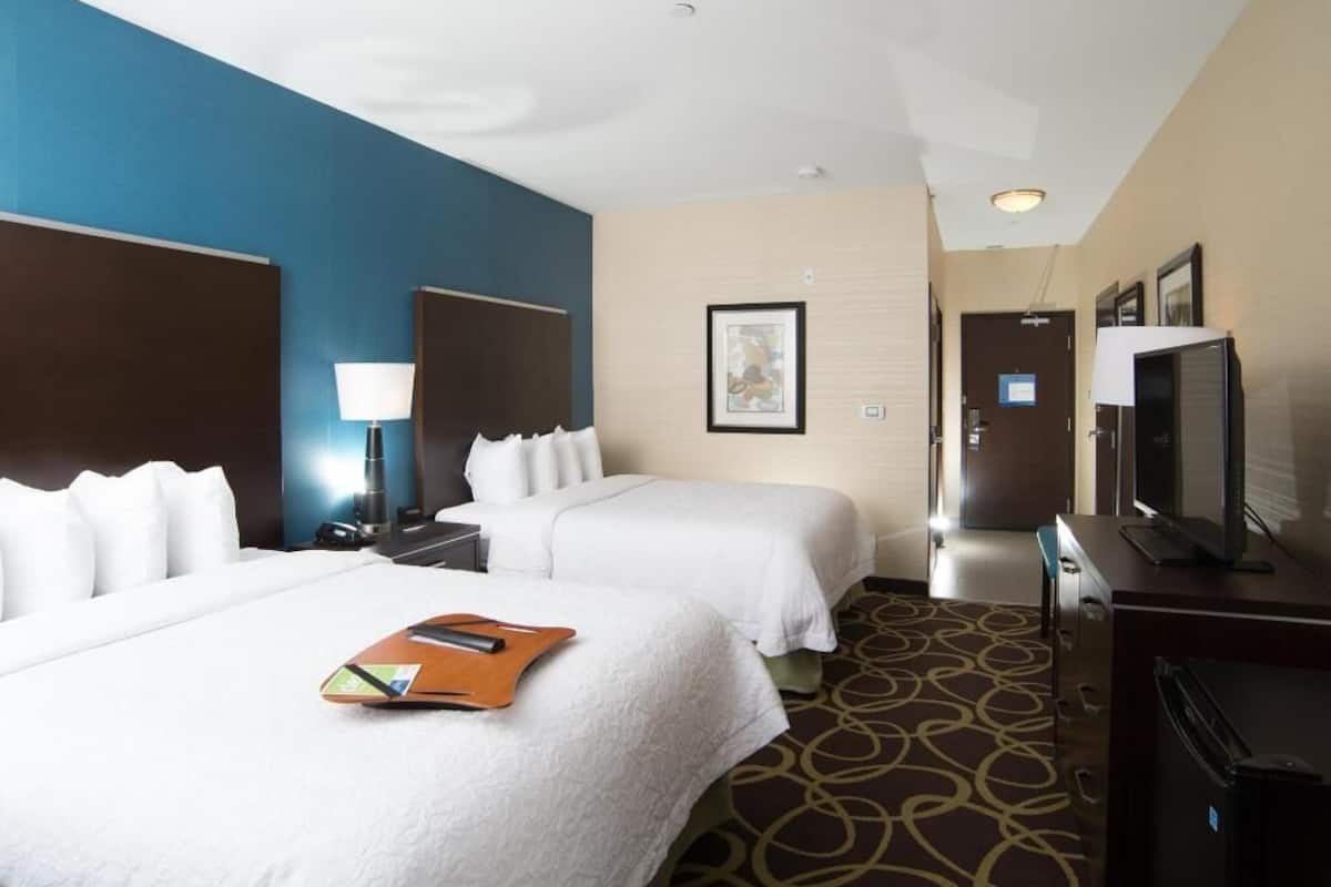 A hotel room with two beds, a desk, a television, and a refrigerator.