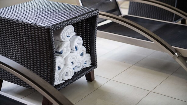 A wicker side table with neatly rolled white towels. - Hampton Inn & Suites by Hilton Regina East Gate (Regina)