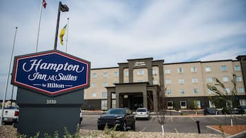 A Hampton Inn & Suites by Hilton sign with a building in the background.