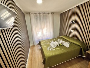 A hotel room with a bed, a TV mounted on the wall, a window with curtains, and a striped wall design. - Hostal Rober (Madrid)