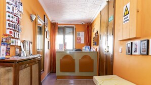 A hotel room with a wooden desk, a bed with a yellow bedspread, a reception desk, and a mirror. - Hostal Rober (Madrid)