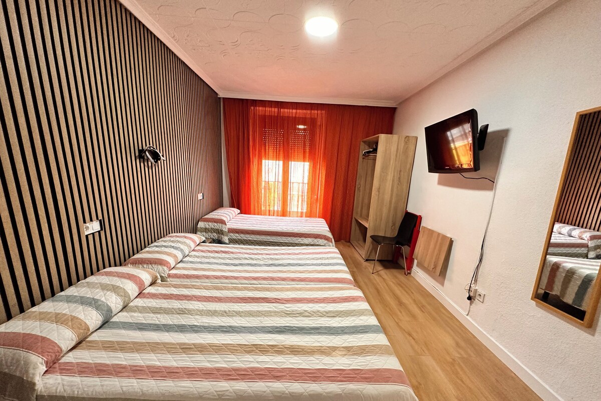 Habitación de hotel con dos camas, un televisor montado en la pared, un armario y un espejo.
