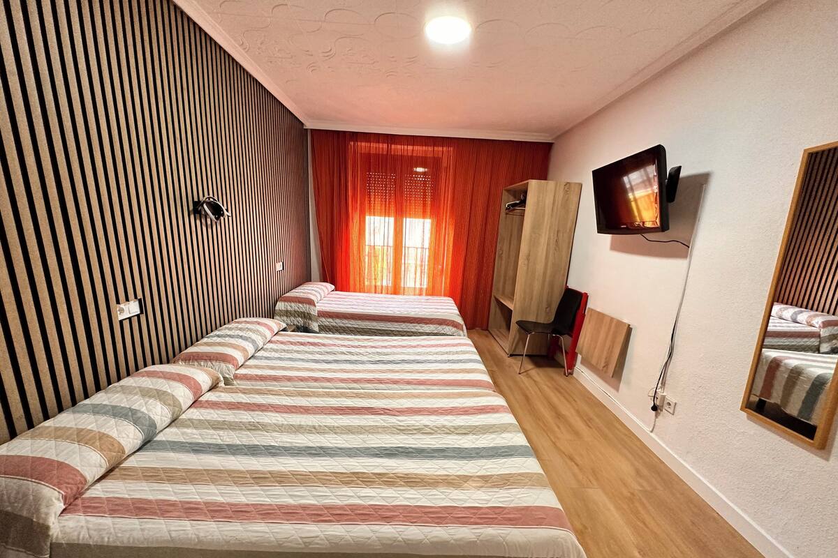 Habitación de hotel con dos camas, un televisor montado en la pared, un armario y un espejo.