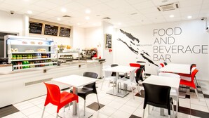 A food and beverage bar with white tables and chairs, a counter with food items, and a menu board. - Design Hostel 101Dalmatinac (Split)