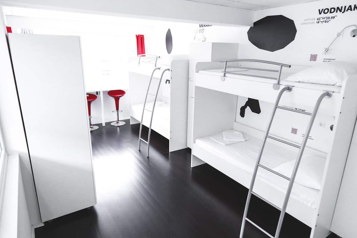 Ein Schlafraum mit Etagenbett, einem weißen Kleiderschrank, einem roten Hocker und einer schwarzen Wanddekoration.