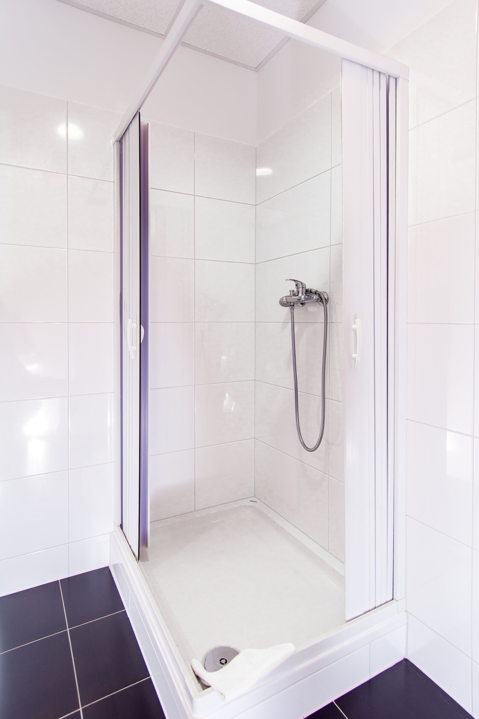 A modern bathroom with a glass-enclosed shower, white tiled walls, and a black floor.