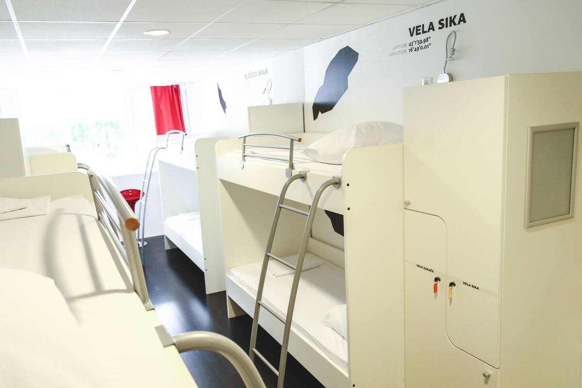 Ein Patientenzimmer mit Etagenbetten, einem roten Vorhang und einer Weltkarte, die Standortkoordinaten zeigt.