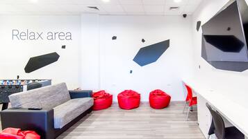 A modern lounge area with a sofa, red bean bags, and a foosball table.