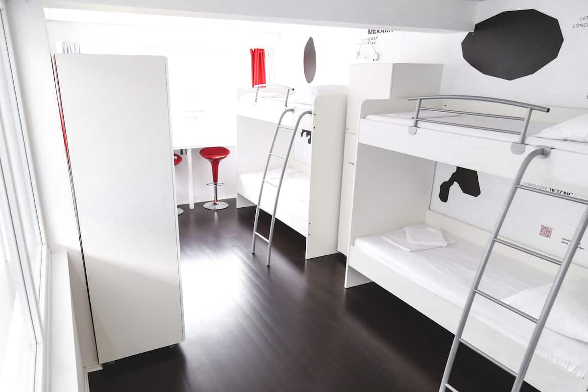 Ein kleines Zimmer mit Etagenbett, einer kleinen Küchenzeile und einem roten Hocker.