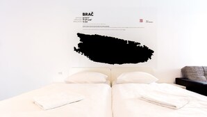 A double bed with white linens and pillows, a black abstract painting on the wall, and a small bedside table with a lamp. - Design Hostel 101Dalmatinac (Split)