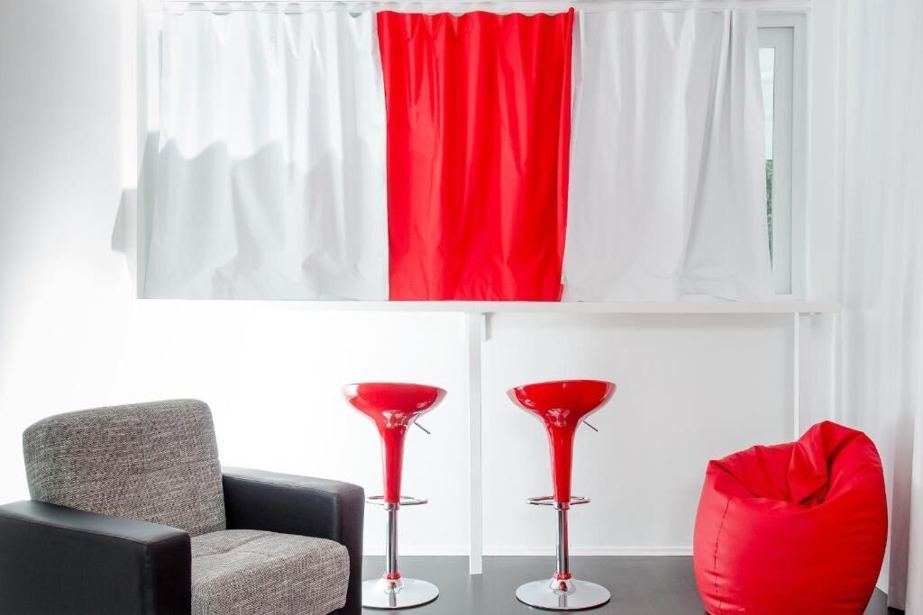 A modern room with a grey armchair, two red bar stools, and a red bean bag chair.