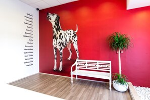 A reception area with a red wall, a white bench, a potted plant, and a wall with a list of languages. - Design Hostel 101Dalmatinac (Split)
