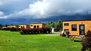 A row of wooden cabins with a grassy lawn and trees in the background. - Motel du Haut Phare (Gaspé)