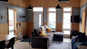 A cozy living room with a grey sofa, a wooden dining table, and a small black heater. - Motel du Haut Phare (Gaspé)