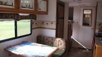 Interior compacto de RV com cozinha compacta, área de refeições com mesa e banco, e janela com vista para o exterior.