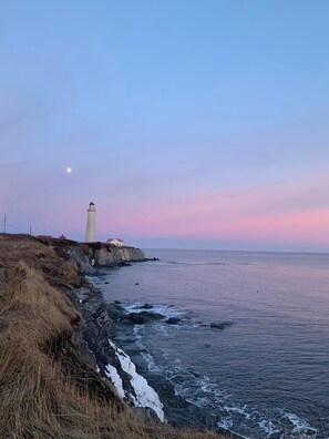A coastal scene with a lighthouse, rocky shoreline, and ocean waves. - Motel du Haut Phare (Gaspé)