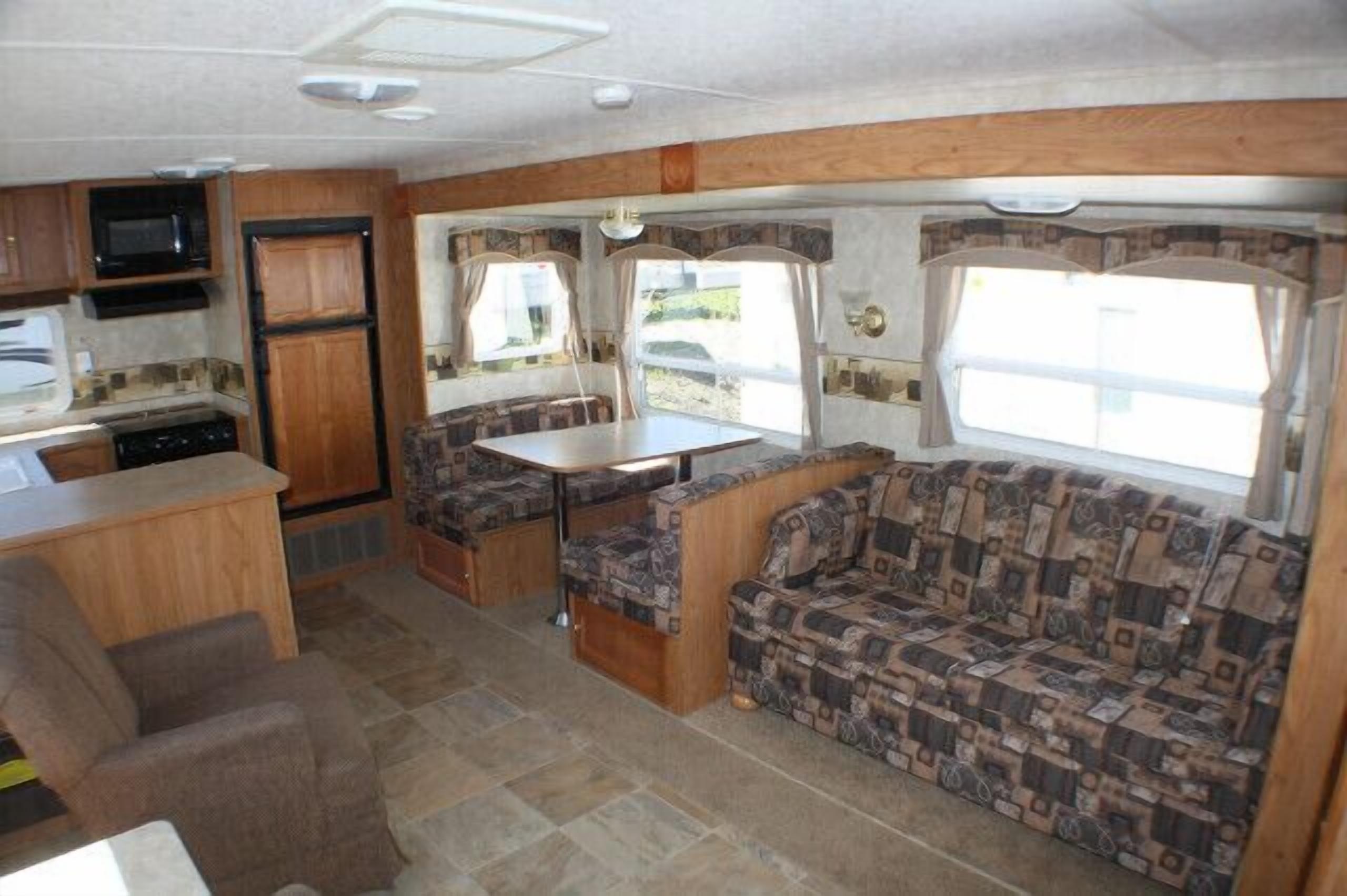 Interior compacto de una caravana con kitchenette, comedor y zona de estar con tapicería estampada.