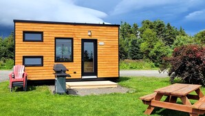A modern wooden cabin with a deck, a barbecue grill, and picnic tables. - Motel du Haut Phare (Gaspé)