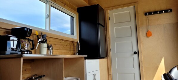 Una cocina compacta con un refrigerador negro, armarios de madera, una ventana y una puerta con un gancho.