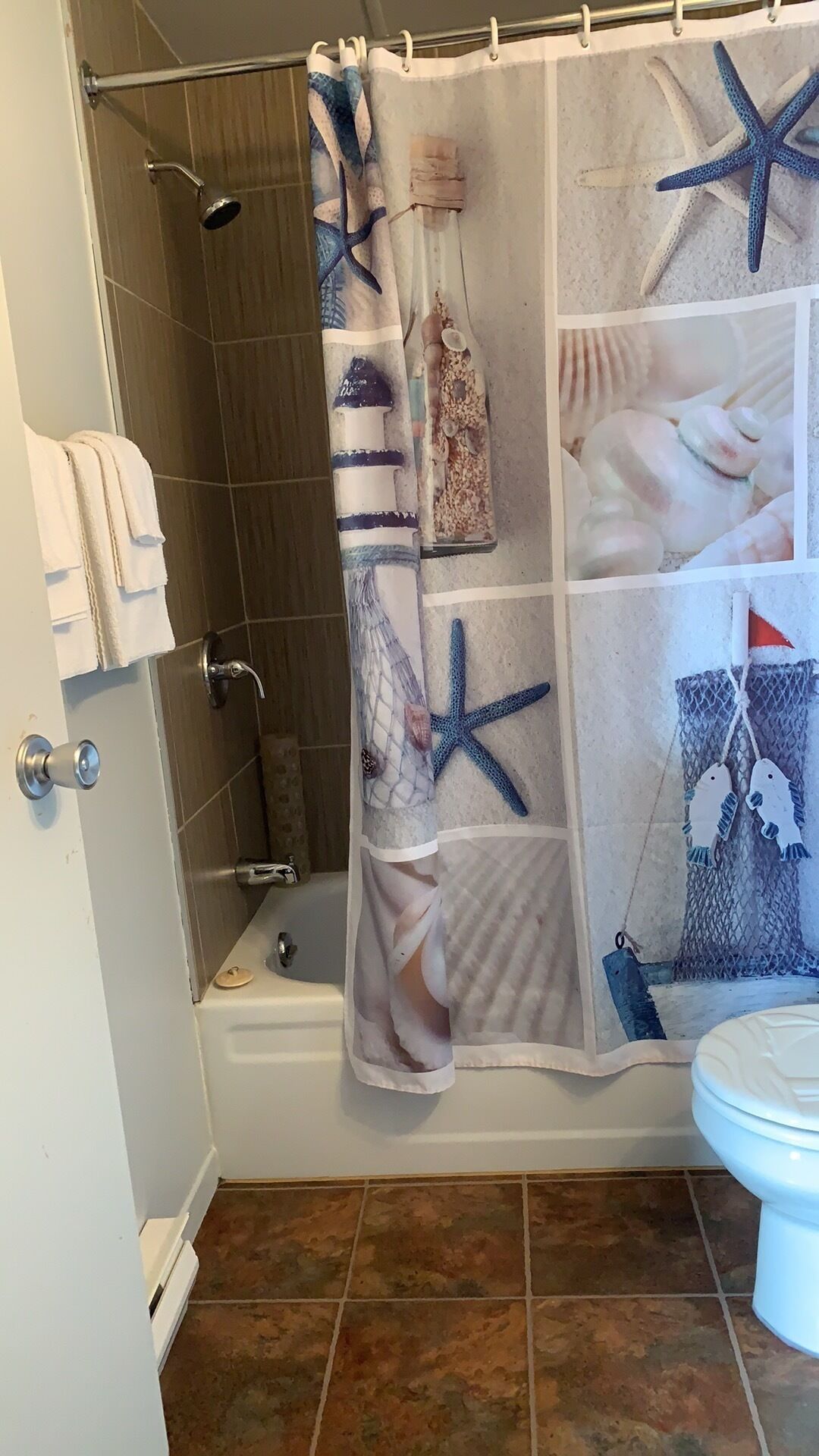 A bathroom with a shower curtain featuring a nautical theme, a toilet, and a towel rack.