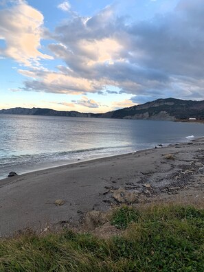 A beach with a rocky shoreline, calm water, and distant mountains under a partly cloudy sky. - Motel du Haut Phare (Gaspé)