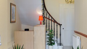 Un pasillo con un candelabro, una recepción, plantas en macetas y una puerta.