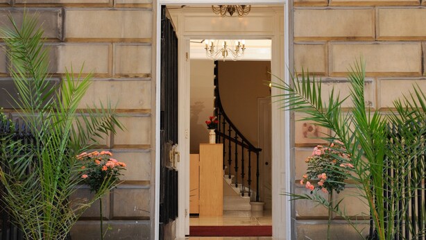 Fachada de piedra con una entrada, una escalera que conduce al interior y plantas en macetas a ambos lados.
