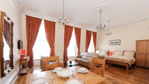Un salón espacioso con una mesa de comedor de madera para cuatro personas, un sofá de cuero, un aparador de madera y un amplio ventanal con cortinas.