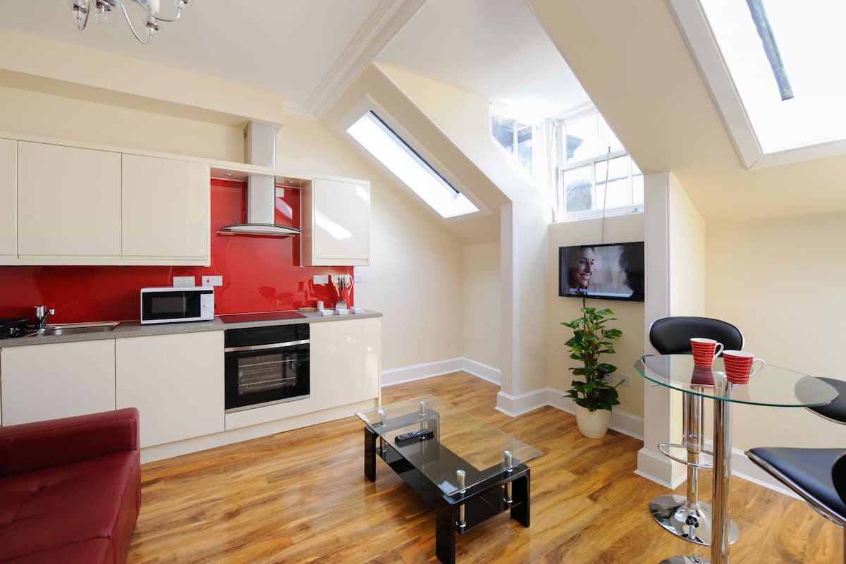 A modern kitchen with white cabinets, a red accent wall, and a skylight.