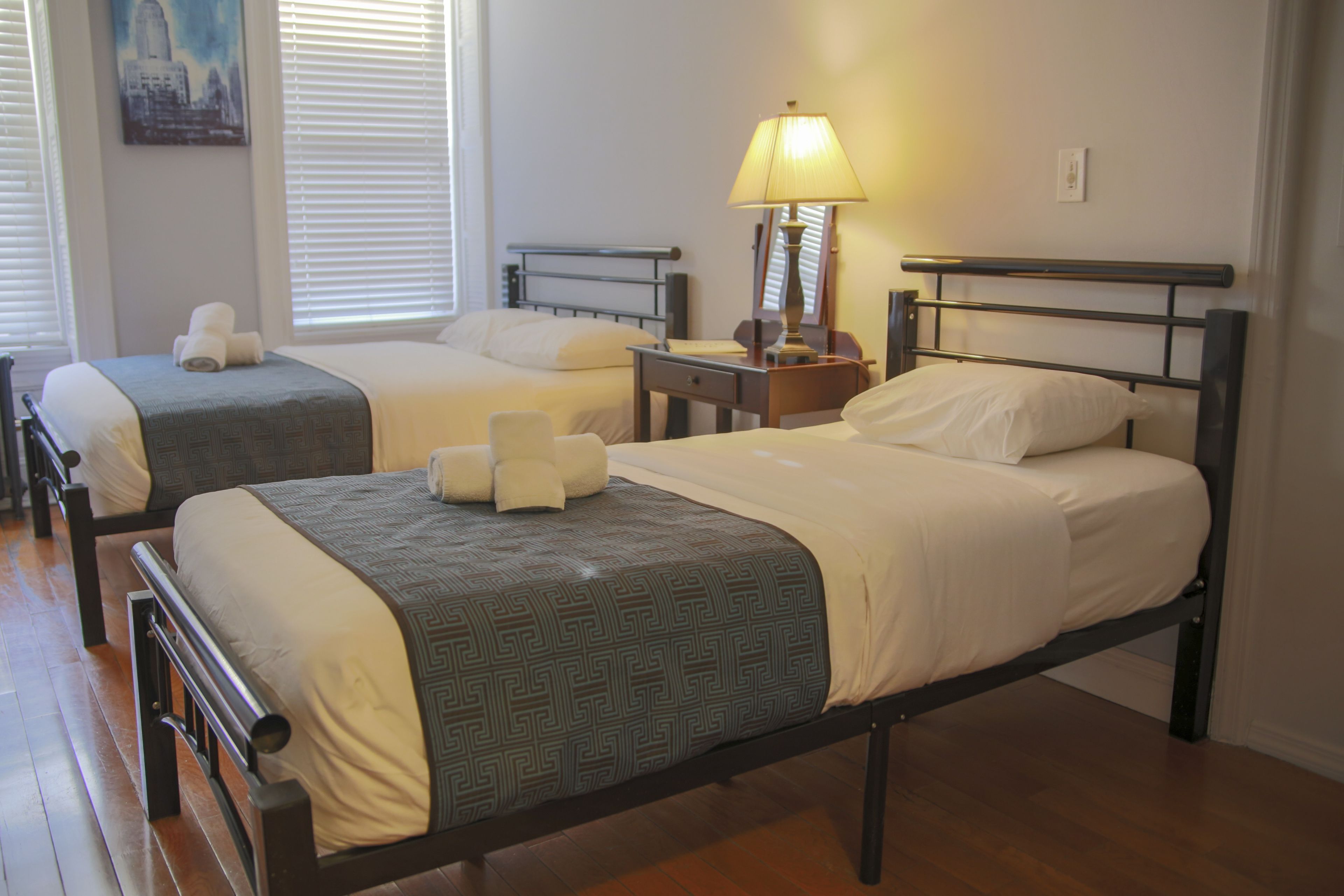 Two single beds with wooden frames and headboards, a bedside table with a lamp, and a painting on the wall.