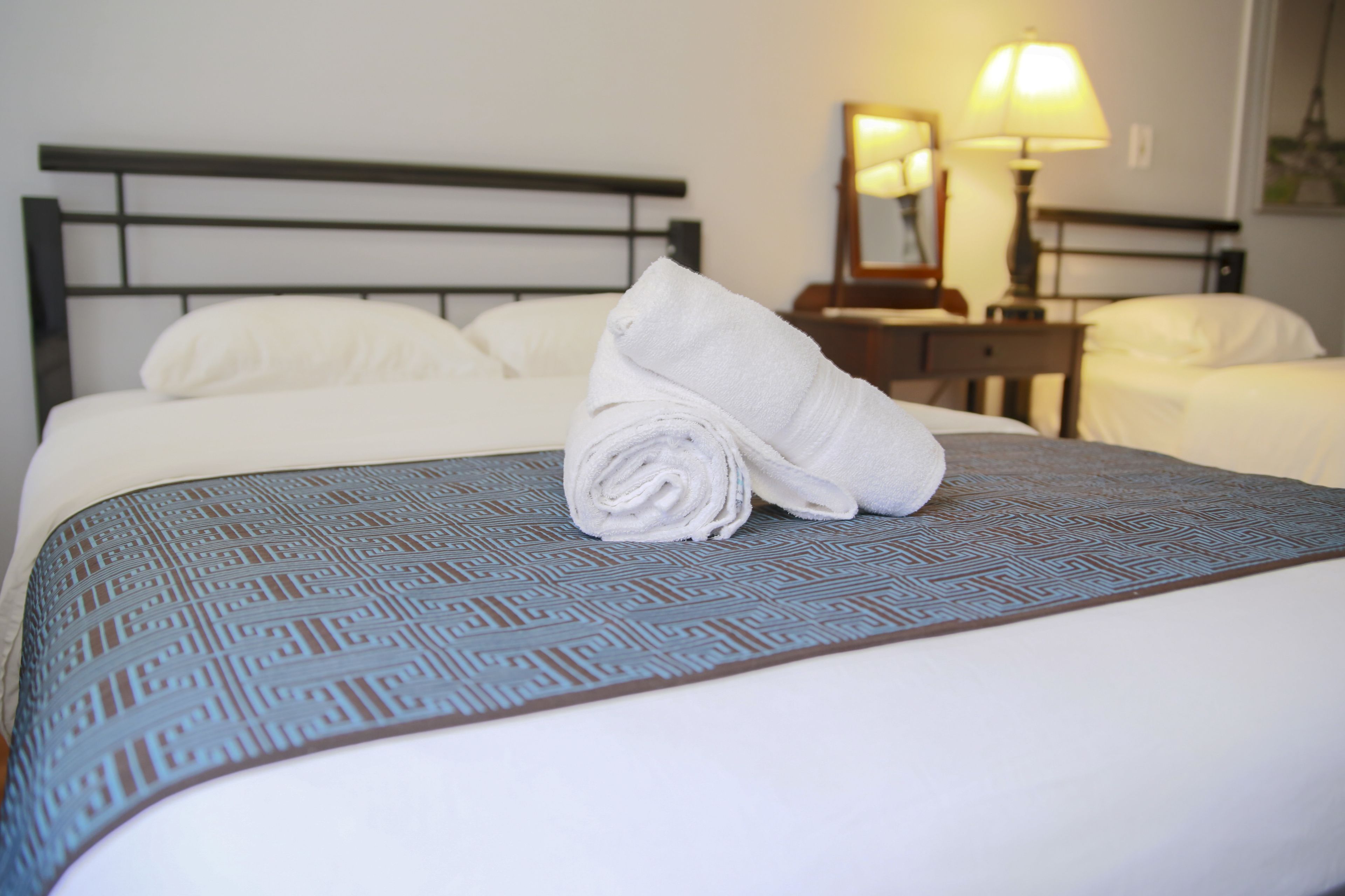 A neatly made bed with a patterned bedspread and a rolled towel on top.