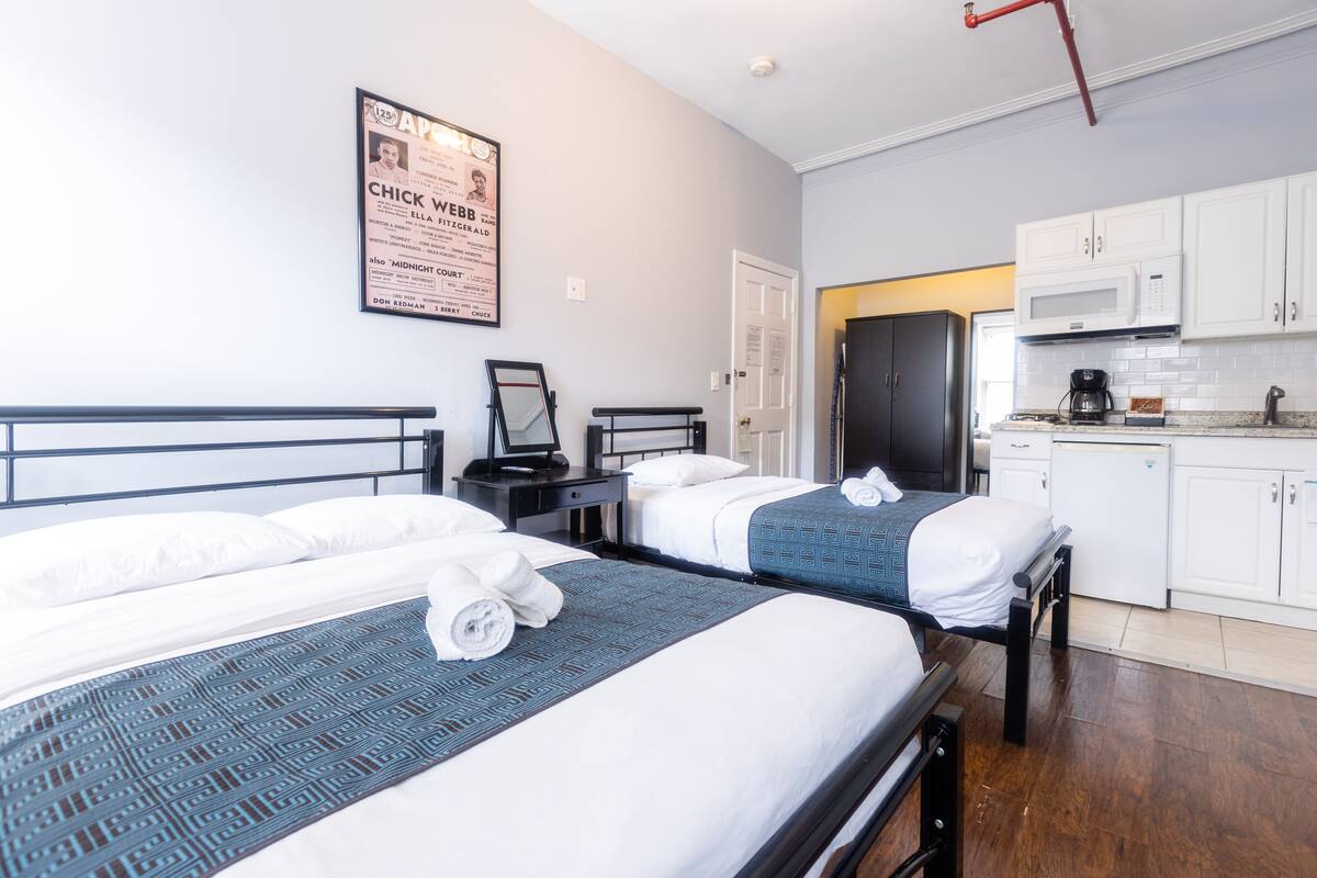 Une chambre d’hôtel avec deux lits, une kitchenette et une affiche au mur.