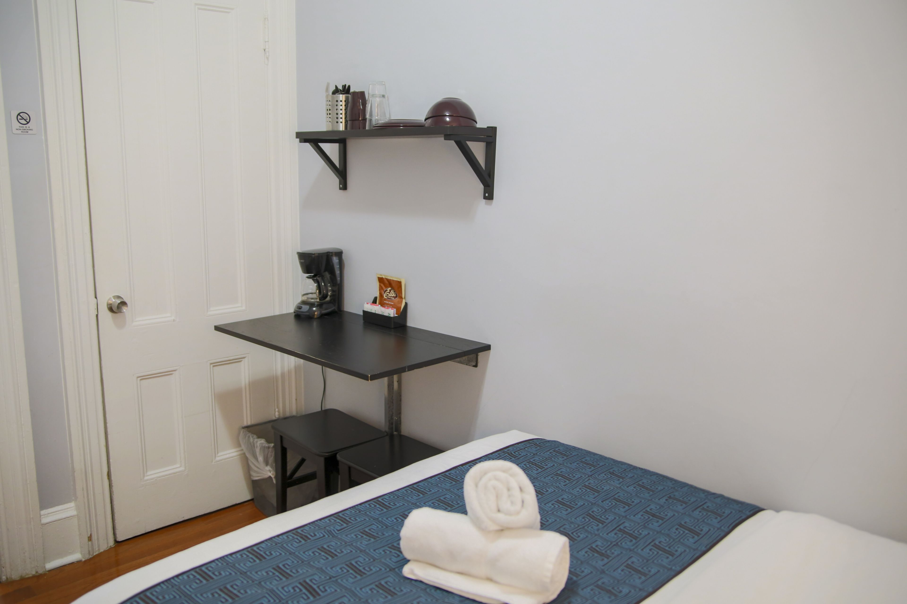 Une chambre comprenant un lit, une petite table, une machine à café et une étagère avec des ustensiles de cuisine.
