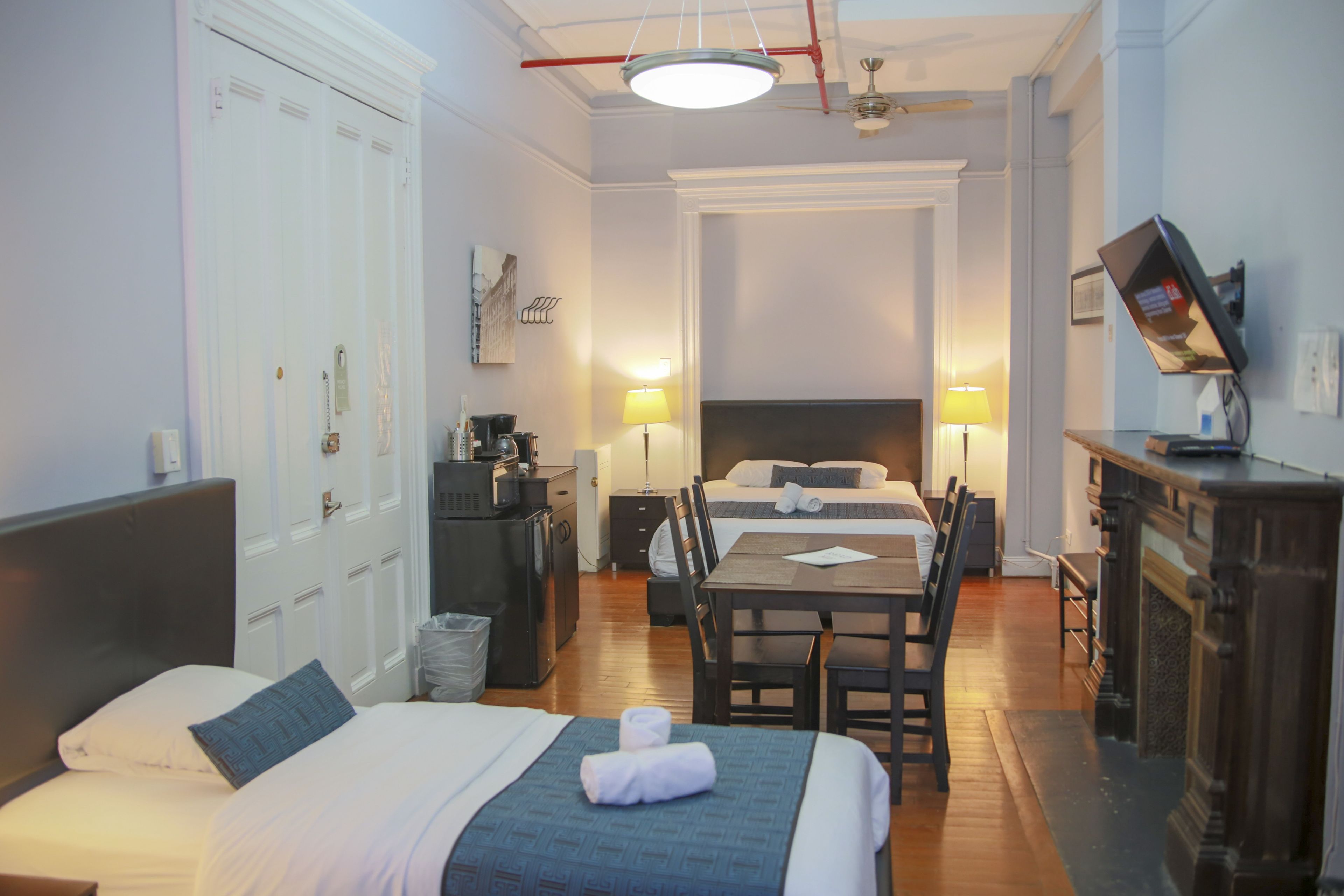 Habitación de hotel con dos camas, una mesa de comedor, sillas, una pequeña cocina y una chimenea.