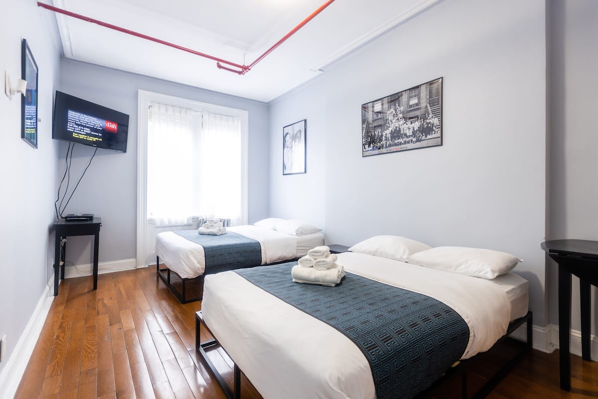 Une chambre d’hôtel avec deux lits, une télévision, une fenêtre avec des rideaux et un tableau encadré au mur.