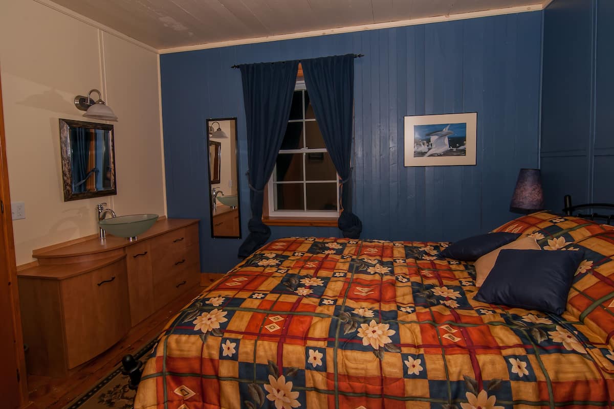 A bedroom with a bed, a dresser, a window with curtains, a mirror, and a picture on the wall.
