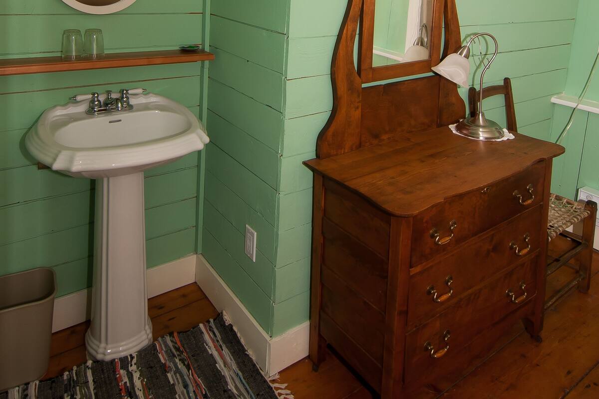 A bathroom with a sink, mirror, vanity, and a wooden dresser.