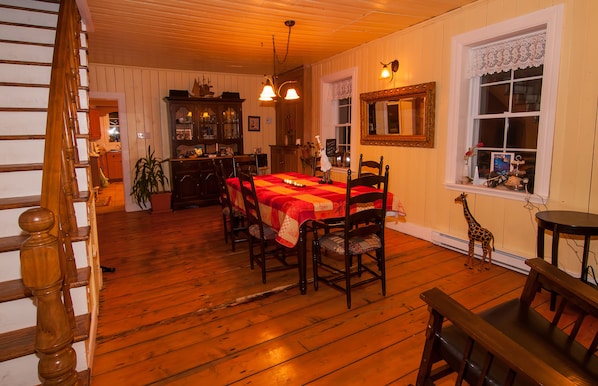 A dining area with a wooden table and chairs, a wooden staircase, and a dining table set with a red tablecloth.