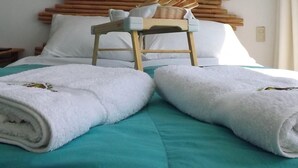 Habitación de hotel con cabecera de madera, una silla de madera y una cama con colcha color turquesa y toallas blancas.