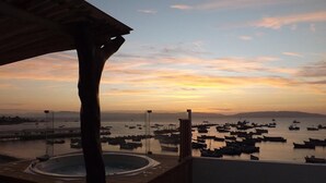 Un jacuzzi en una terraza de madera con vista a barcos y al atardecer sobre el agua.
