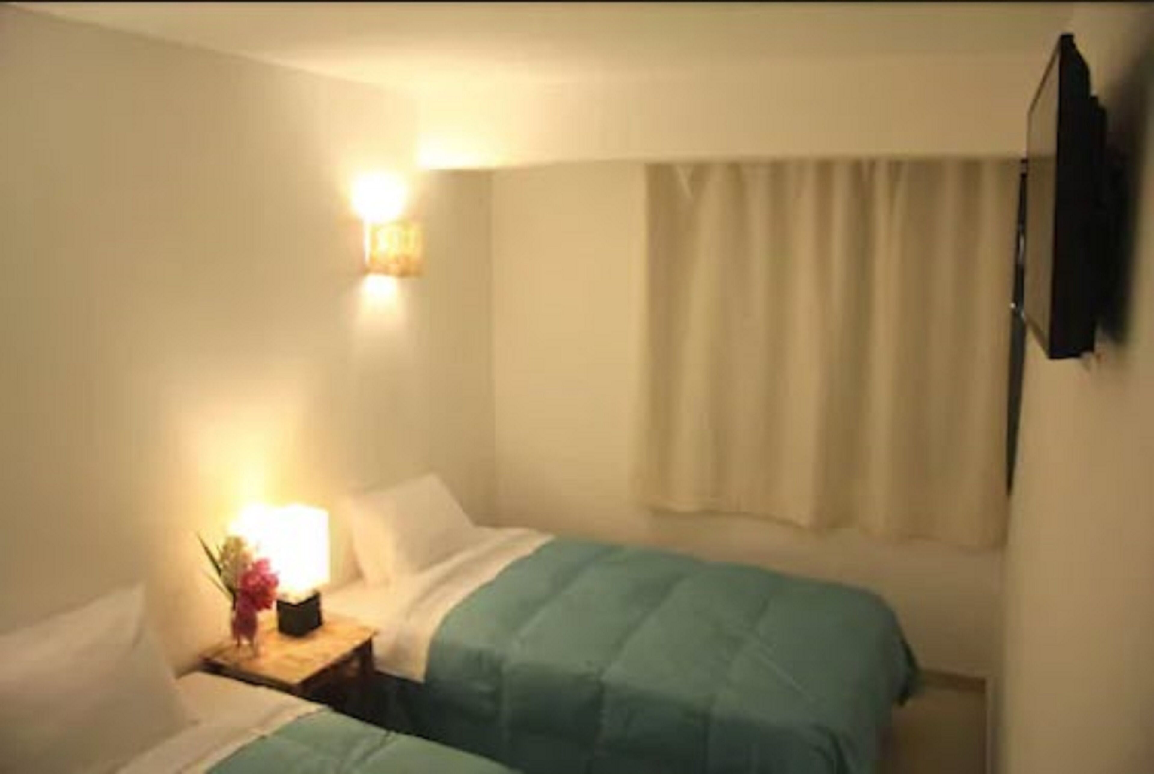 A small, single-bed room with a bedside table, a lamp, and a curtain.