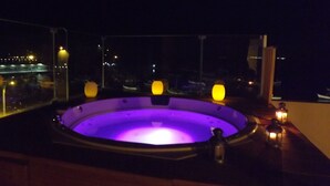 Un jacuzzi con interior morado, rodeado de barandillas de madera, con vistas a un paisaje urbano nocturno.